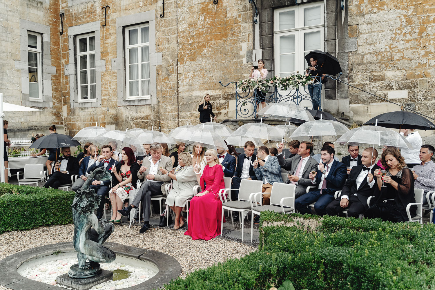 Guests seating at wedding ceremony with wedding transparent and black umbrellas in a terrace of the castle in Limburg.