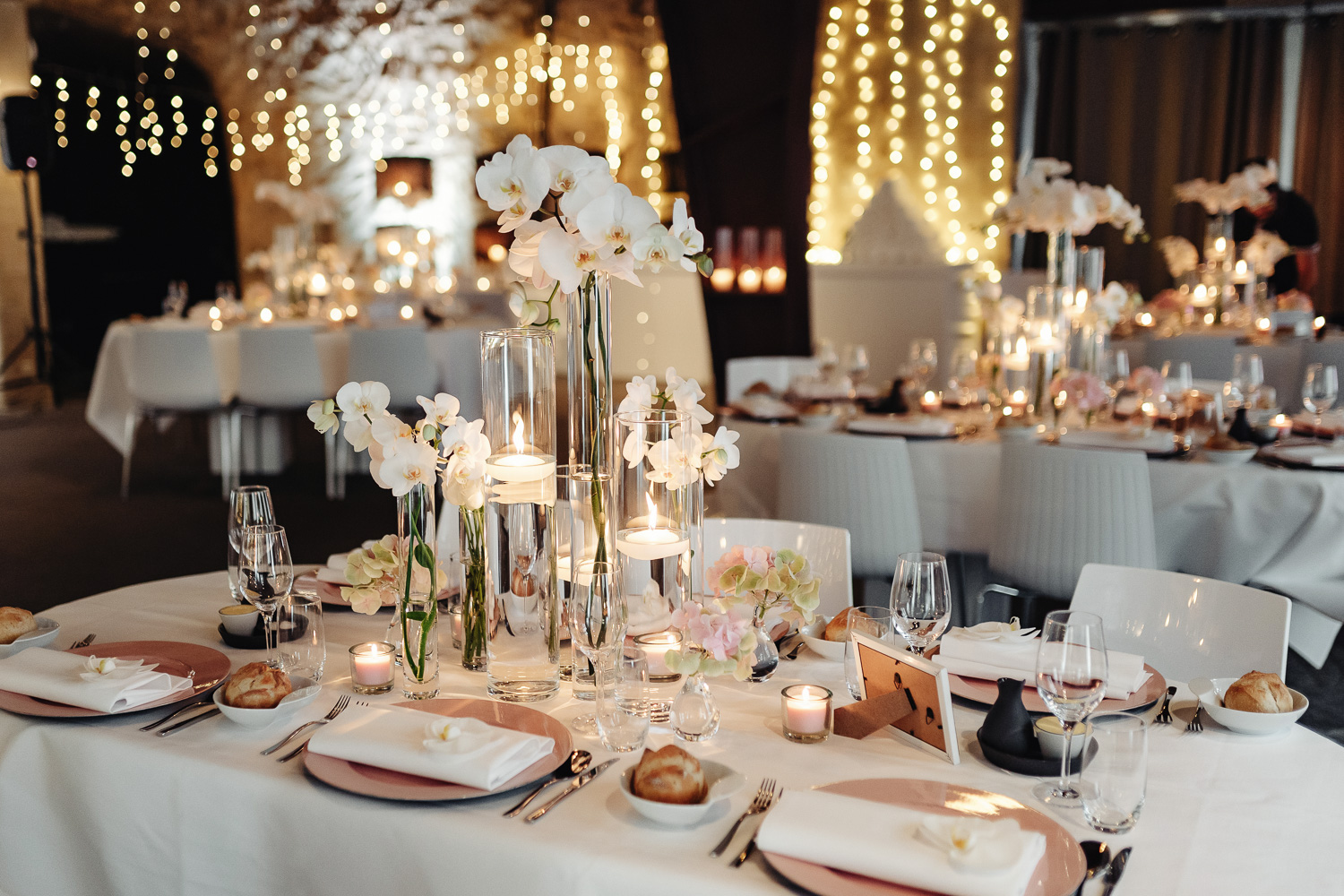 Bruiloft decoratie. Plates laying down at table with names of guests, candle lights and vases, white orchids and light girlands